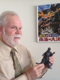 Photo Of Prof. Frank L. Chance Holding A Figure Of Godzilla In Front Of Poster 