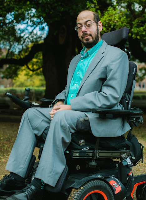 Mark Bookman, sitting tall in his wheelchair, outdoors in front of a tree.